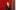 Sally Tallant standing and smiling in front of a red wall, wearing a dark green suit jacket