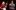 Two presenters on a dark stage with Christmas lights: a blonde woman in a red dress and a man with a beard and glasses in a Fulham Football Club Christmas sweater.
