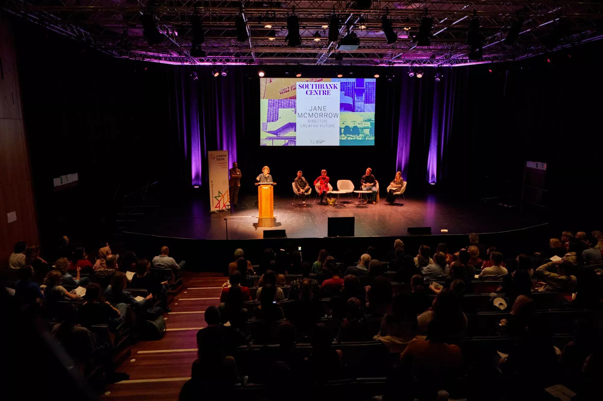 Panel discussion happening on the Purcell Room stage, with a full audience.