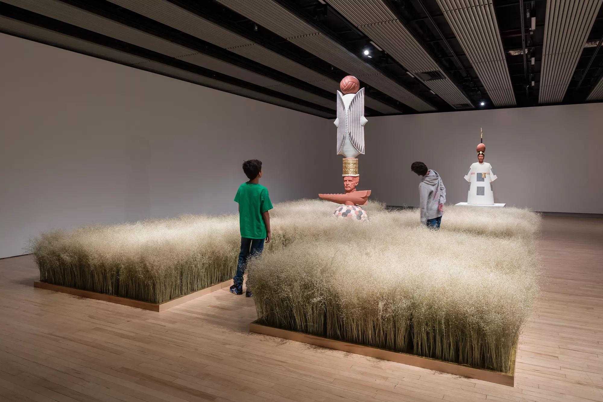 An installation view of a rice field, with sculptures in the middle, and two young children looking at the artwork.