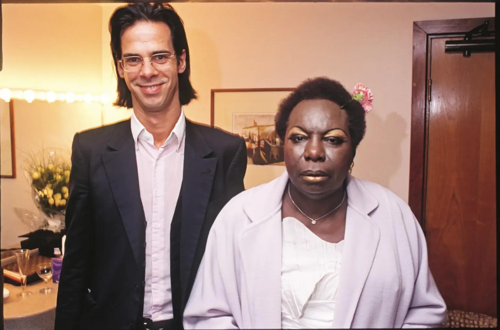 Nick Cave, a tall white man with long dark hair, and Nina Simone, an older Black woman with short dark hair, stand next to each other in a dressing room, backstage in the Royal Festival Hall