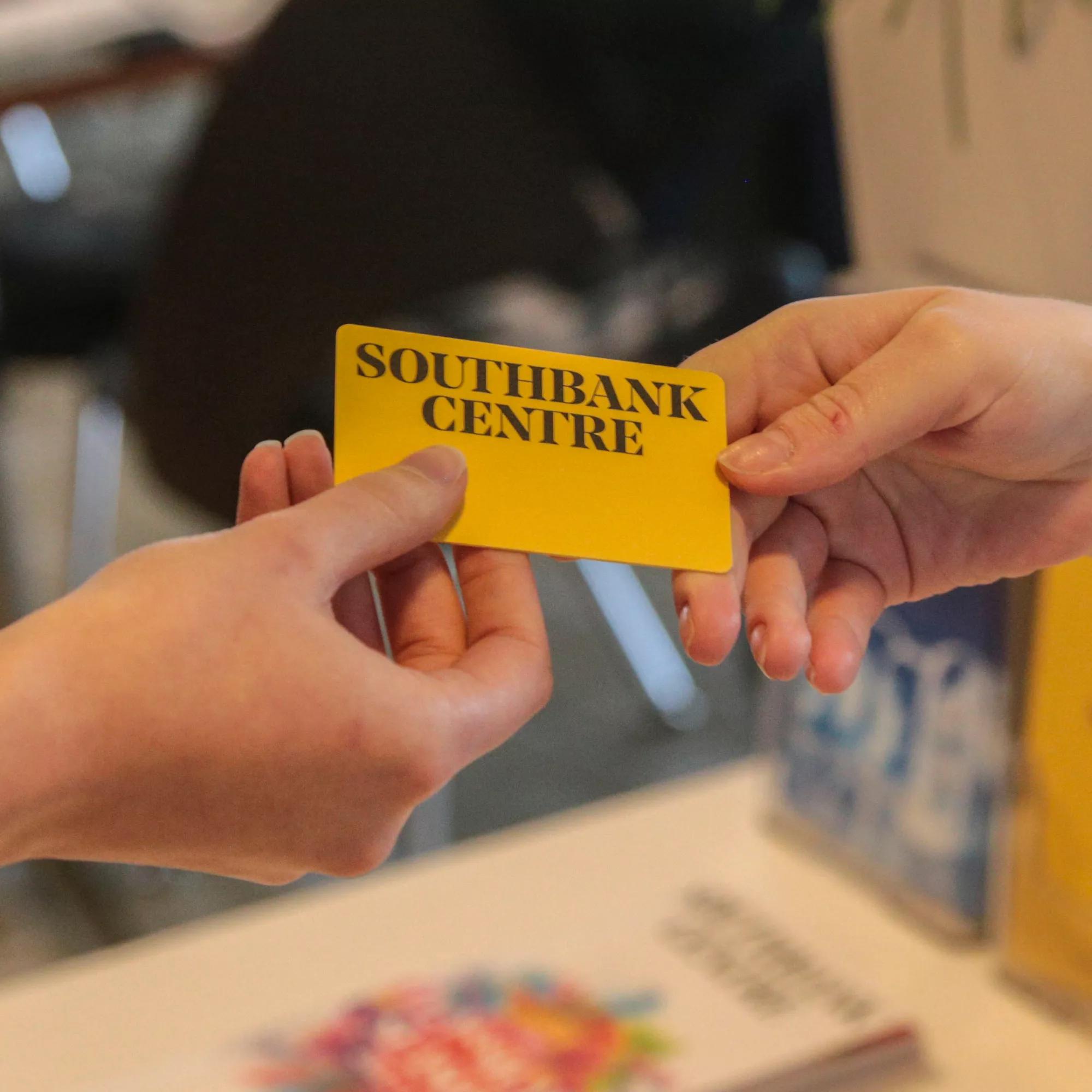 A yellow Southbank Centre Membership card  is held between the hands of two different people