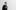 A black and white, slightly blurred full-body photo of a man in glasses and dark clothes walking across a white background.