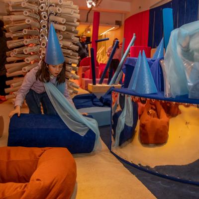 A woman and child poking their heads through a furry orange doughnut-shaped circle