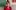 A woman in a red blouse sat smiling at the camera, she wears dark round glasses